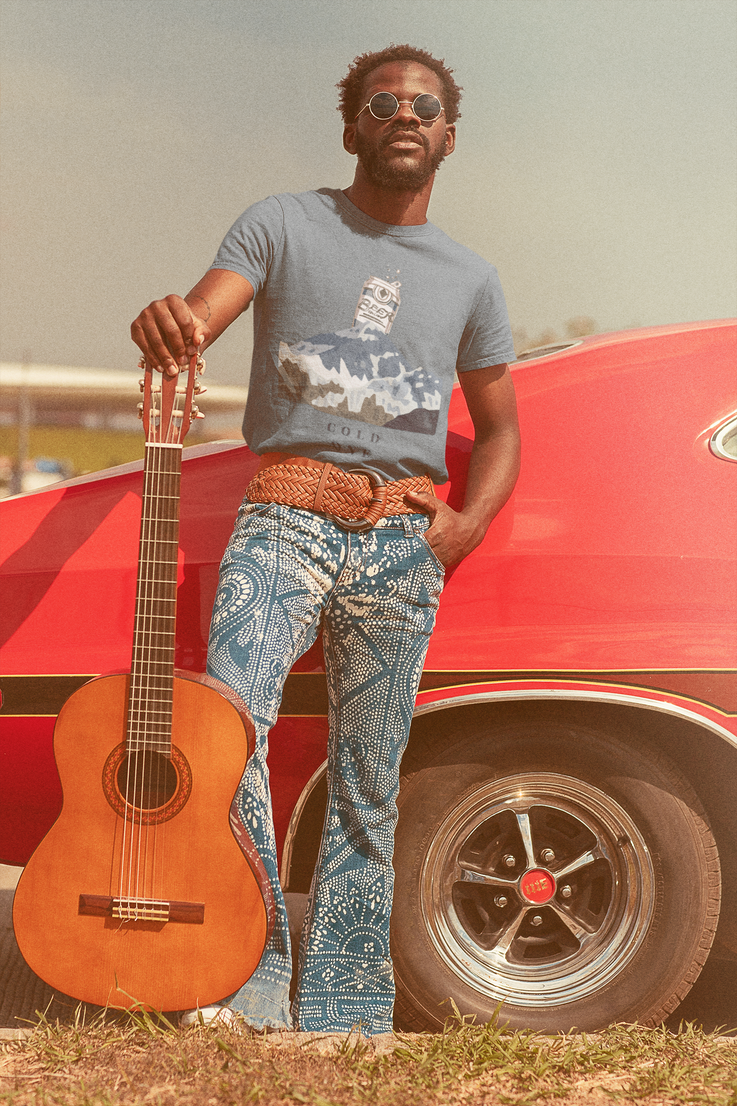 Man holding a guitar in front of a red car with a blurred background