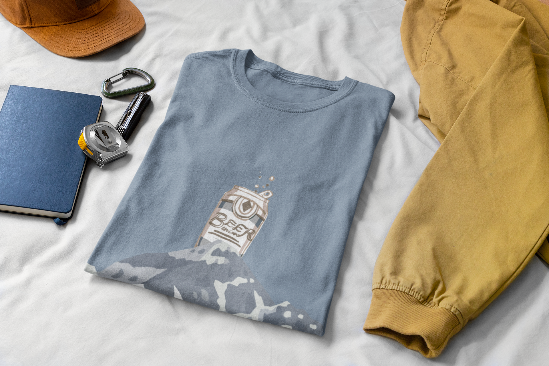 Folded blue t-shirt with graphic design on a white surface, next to a yellow shirt and accessories.
