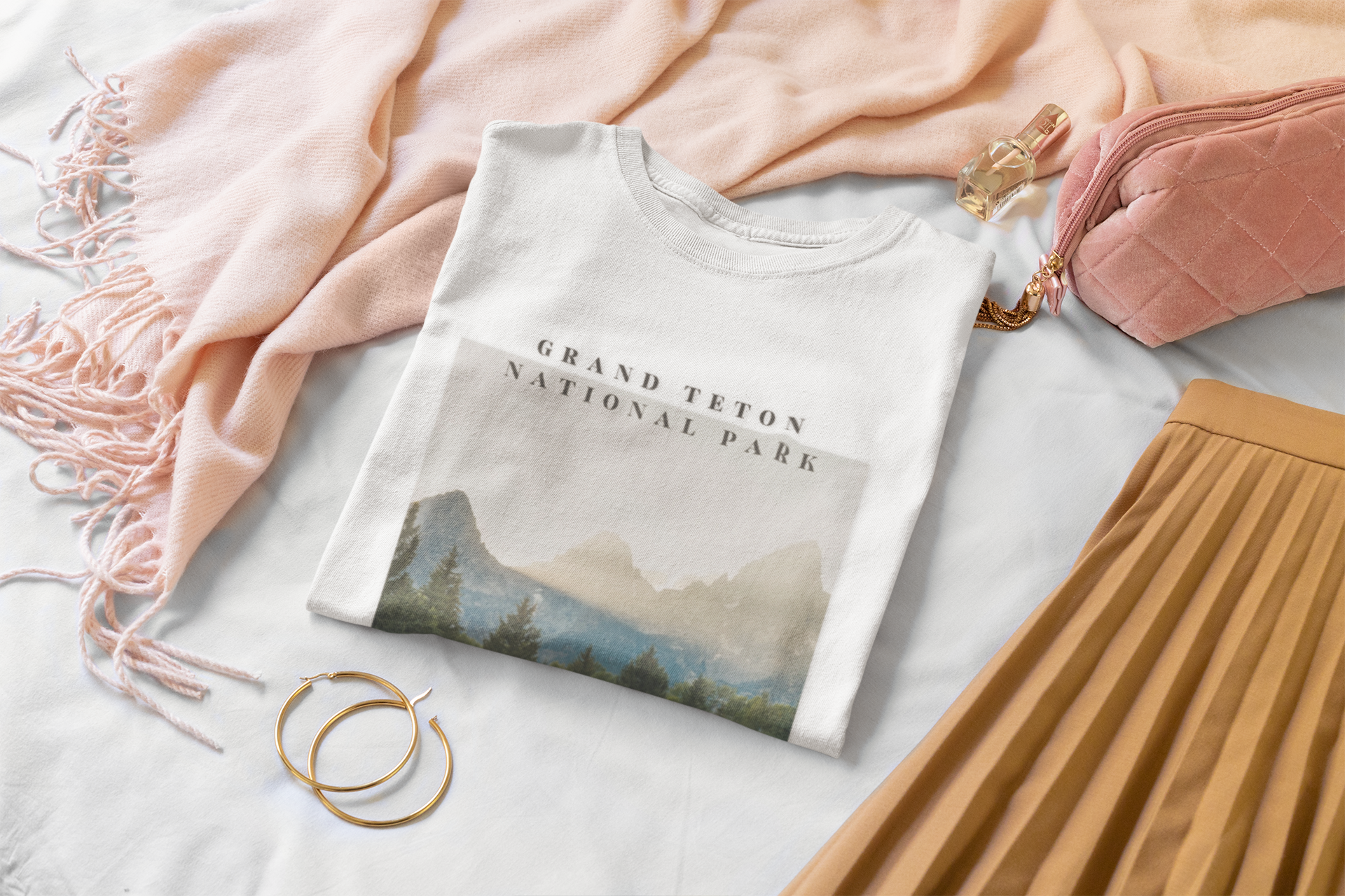 Folded t-shirt with 'Grand Teton National Park' design on a light surface with a pink blanket and brown skirt.
