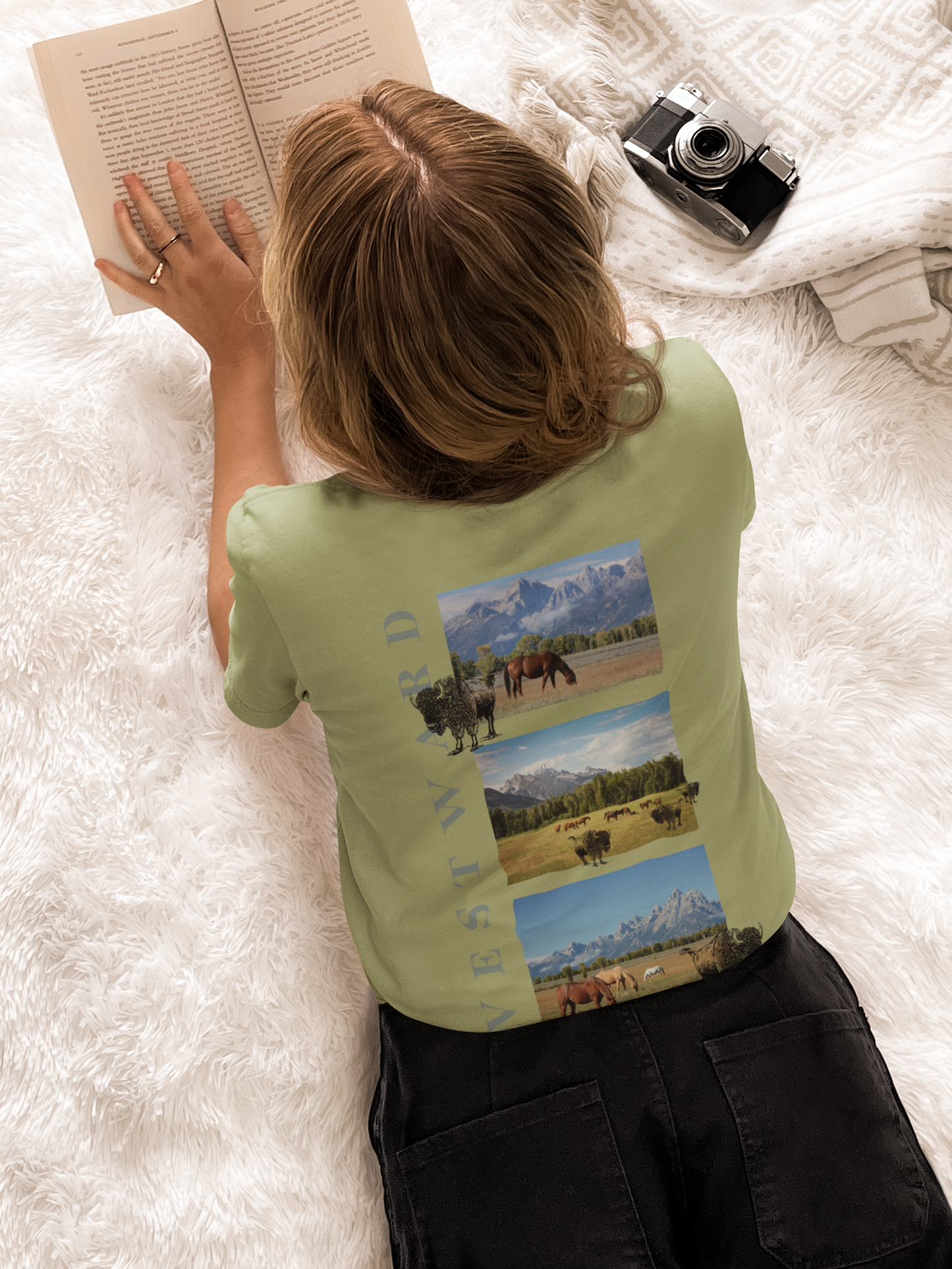 Person wearing a green t-shirt with a nature-themed design, lying on a white surface and reading a book.