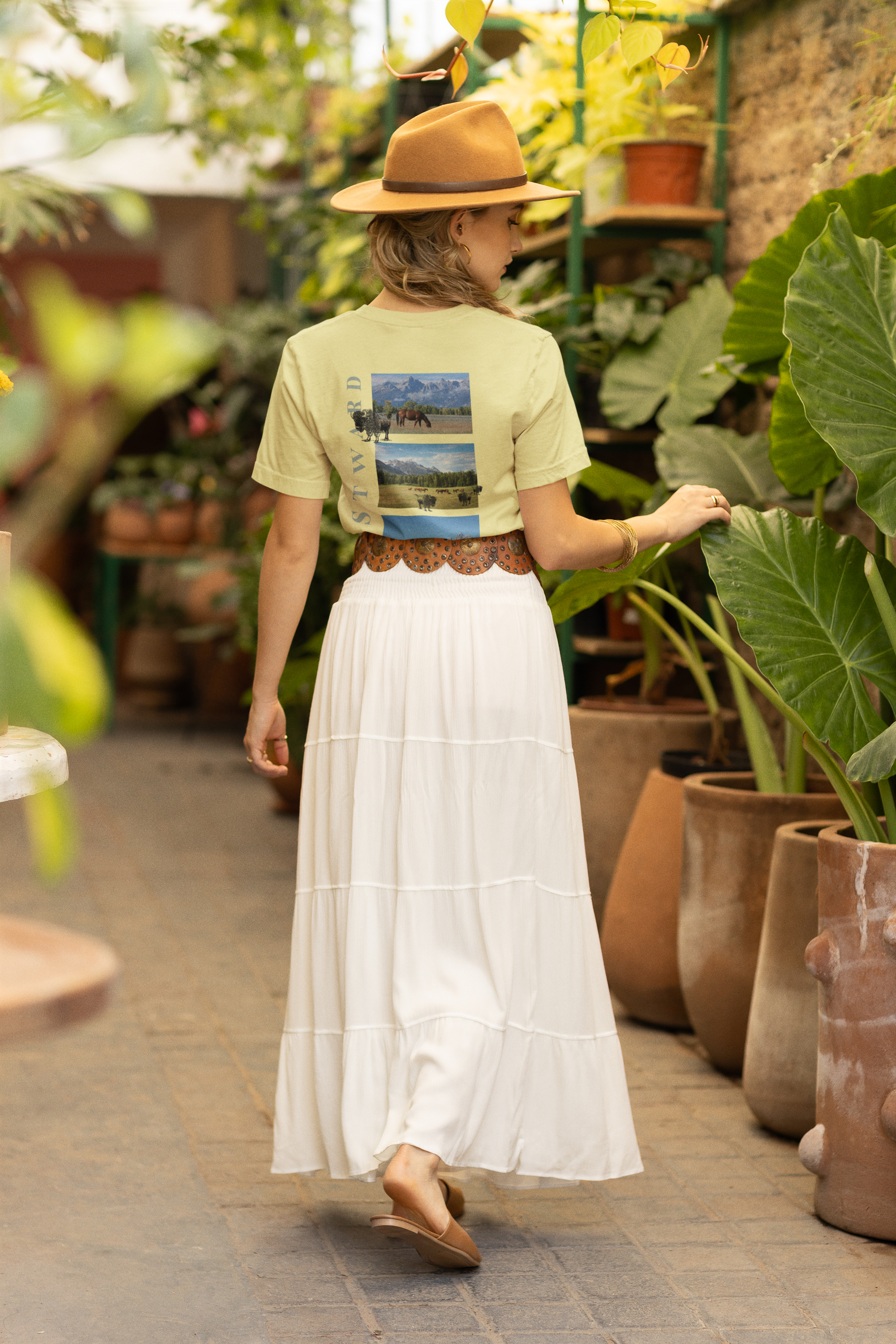 Person wearing a light green shirt with a scenic print and white skirt in a greenhouse setting.